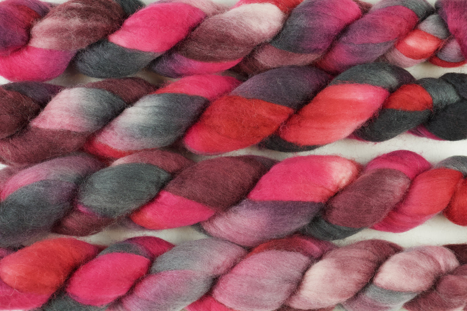 Braided fiber skein with pink, red, and black on a white background