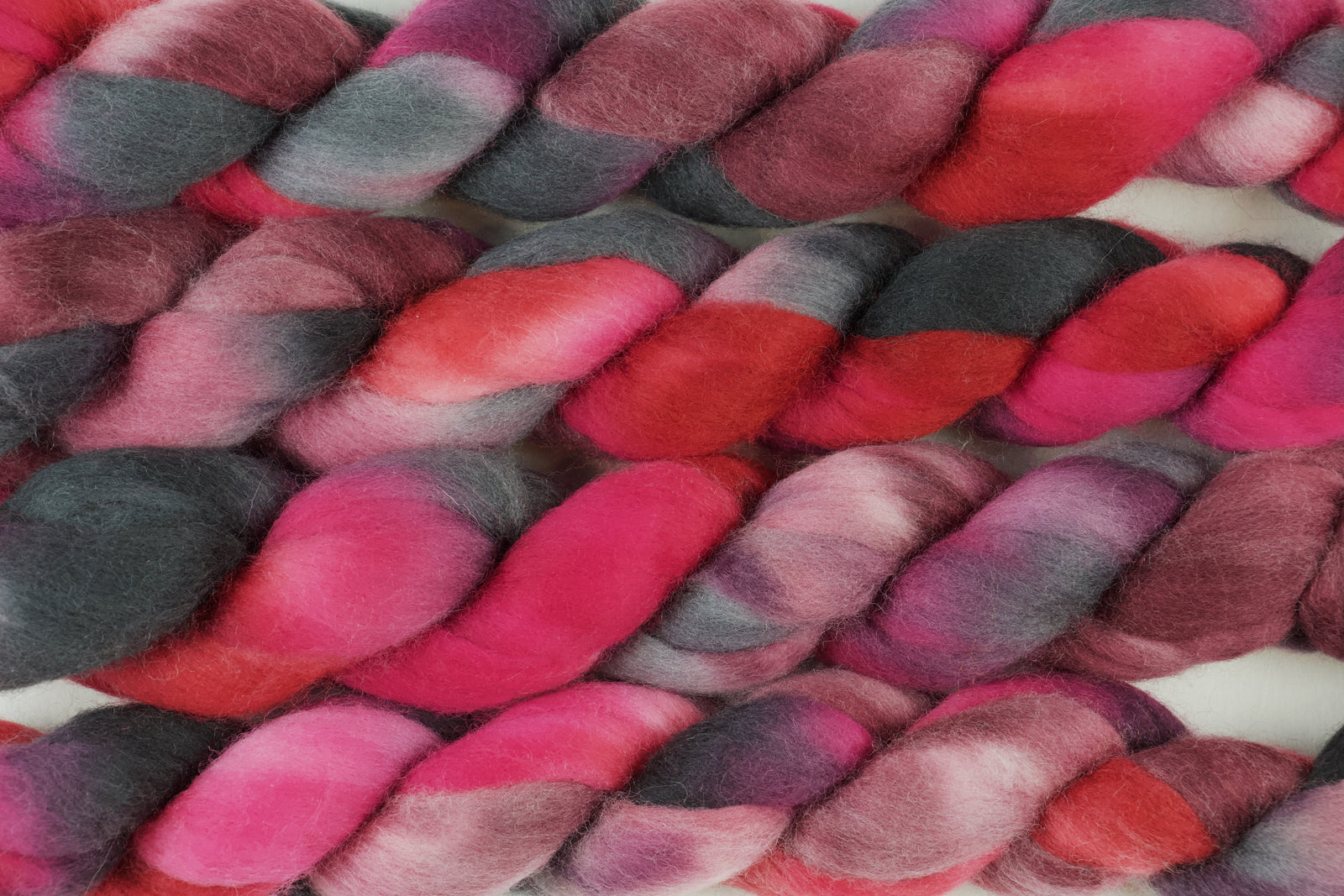 Braided fiber skein with pink, red, and black on a white background