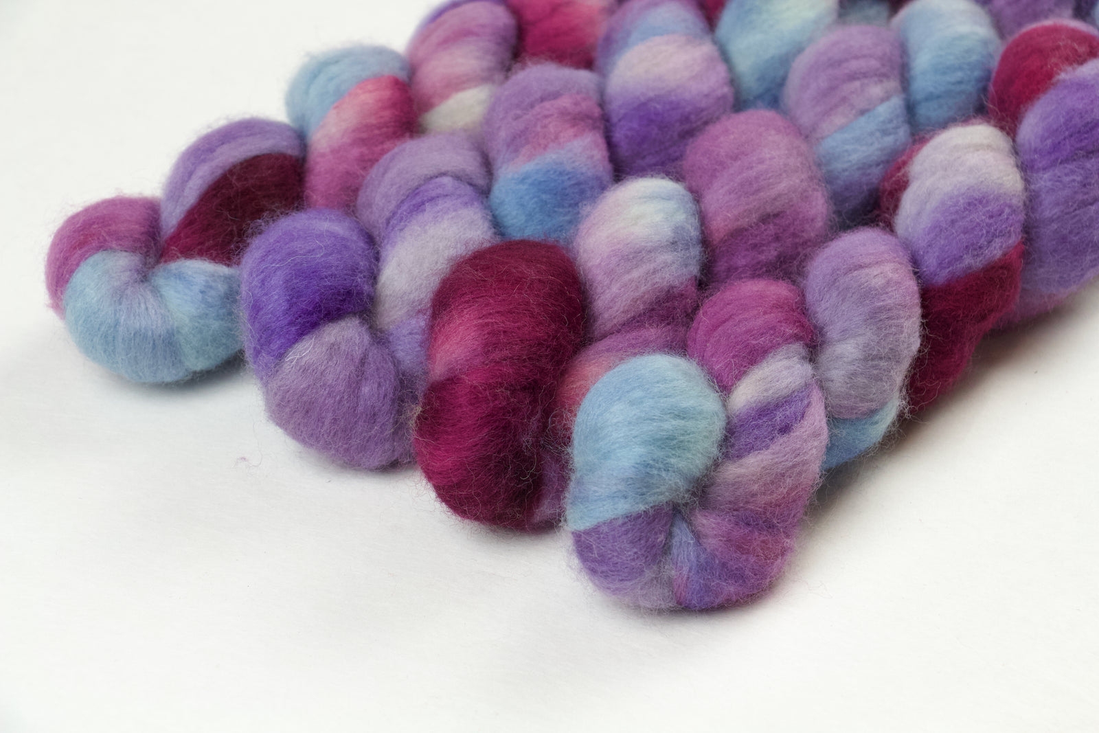 Braided fiber skein with blue, purple, and pink on a white background