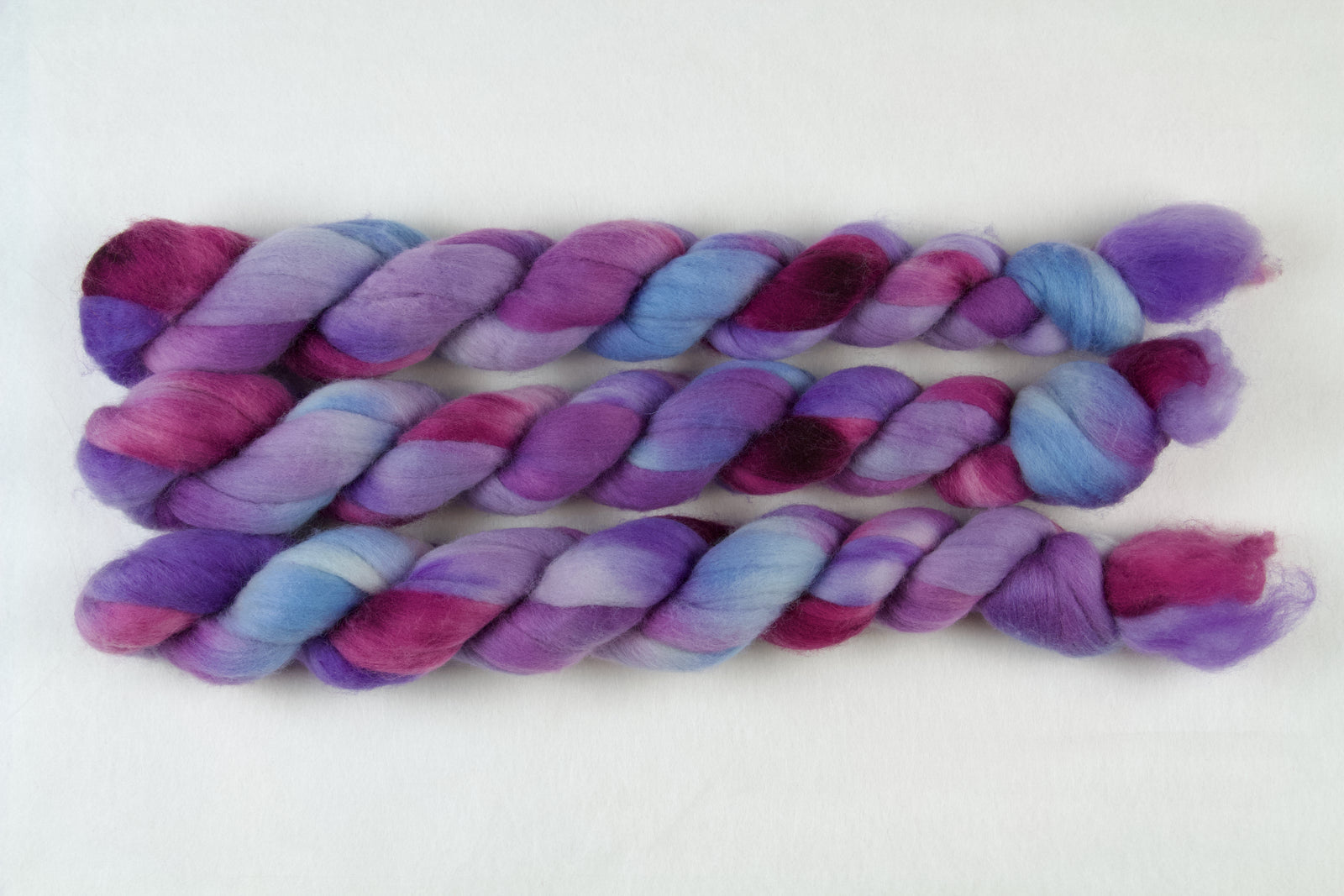 Braided fiber skein with blue, purple, and pink on a white background