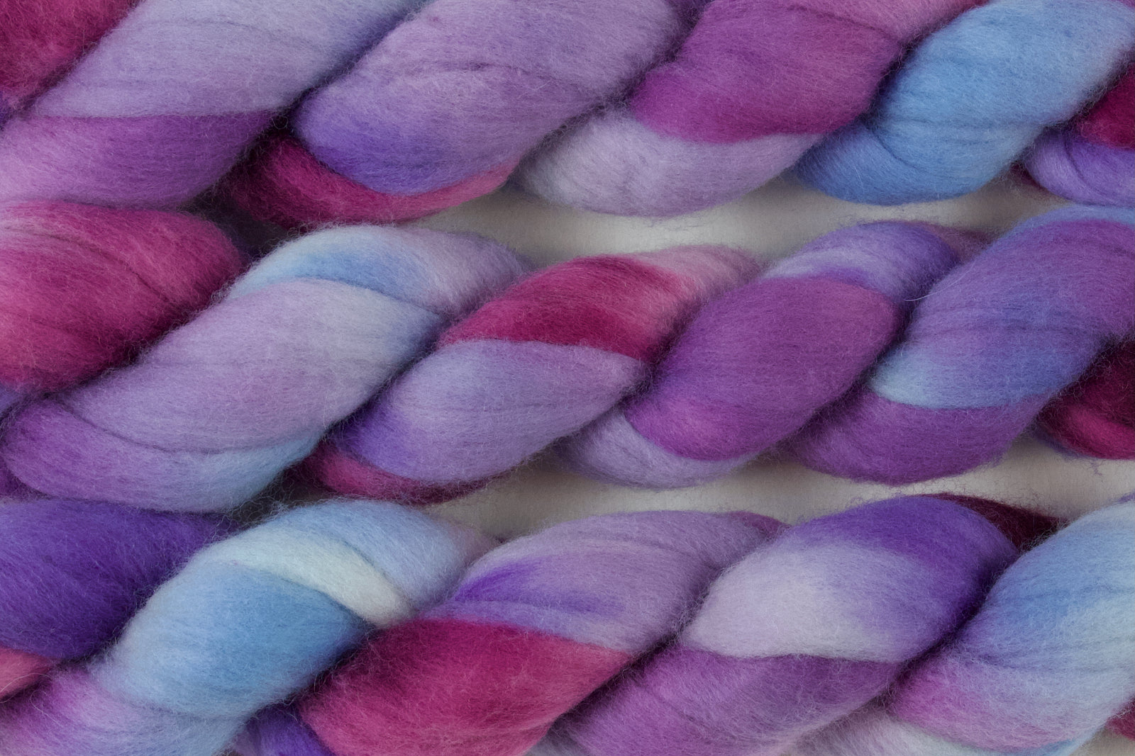 Braided fiber skein with blue, purple, and pink on a white background
