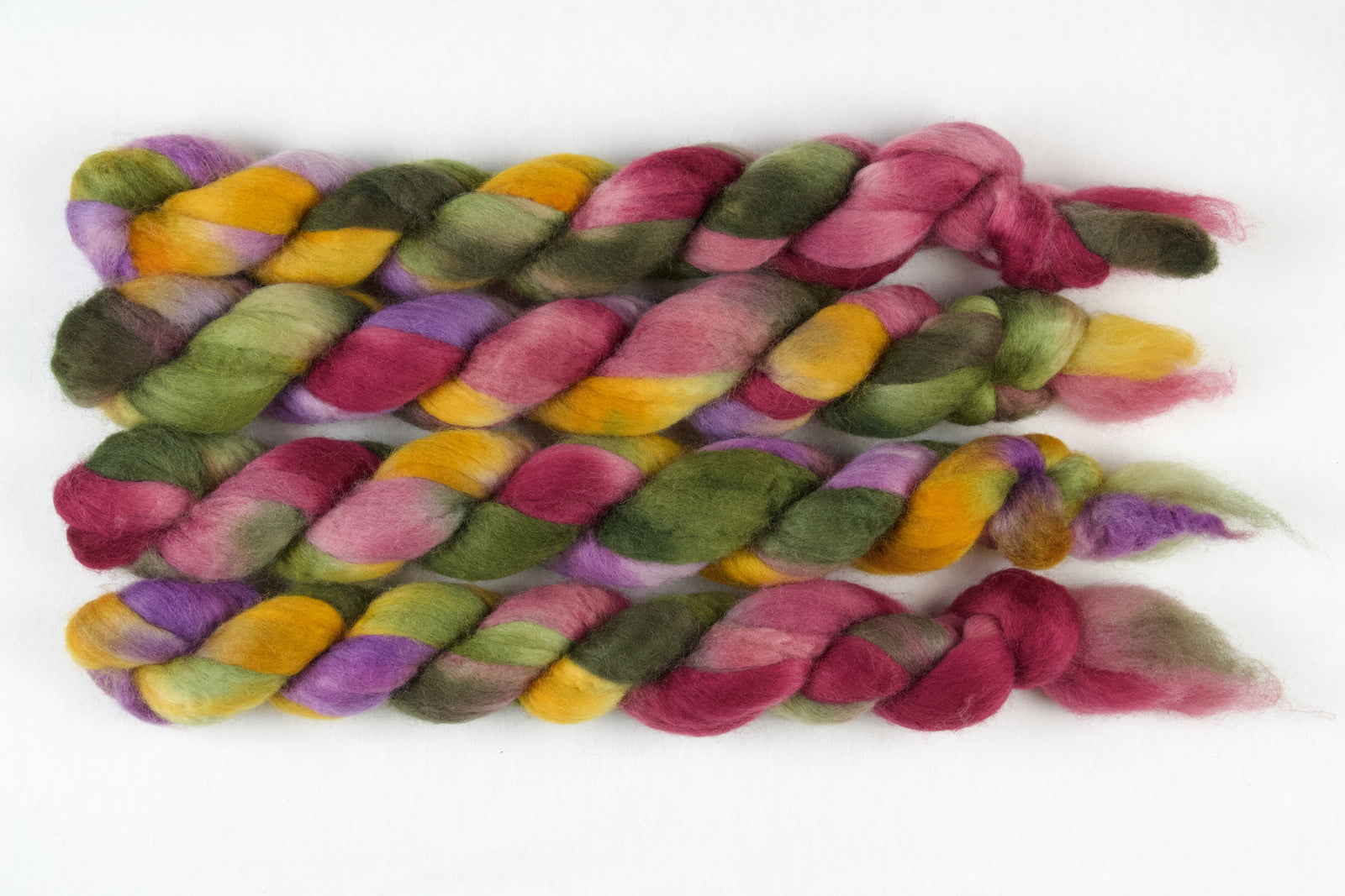 Braided fiber skein with green, pink, purple, and gold on a white background