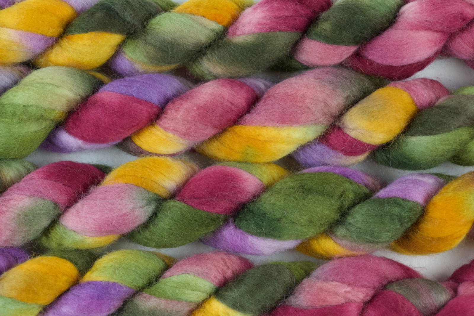 Braided fiber skein with green, pink, purple, and gold on a white background