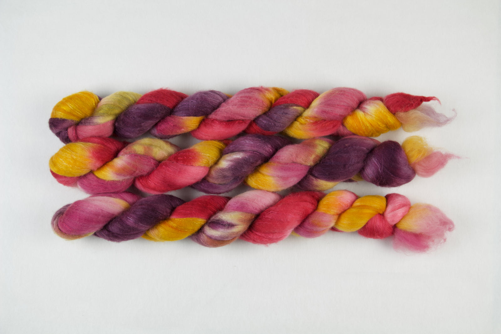 Braided fiber skein with purple, red, pink, mustard, and gold on a white background