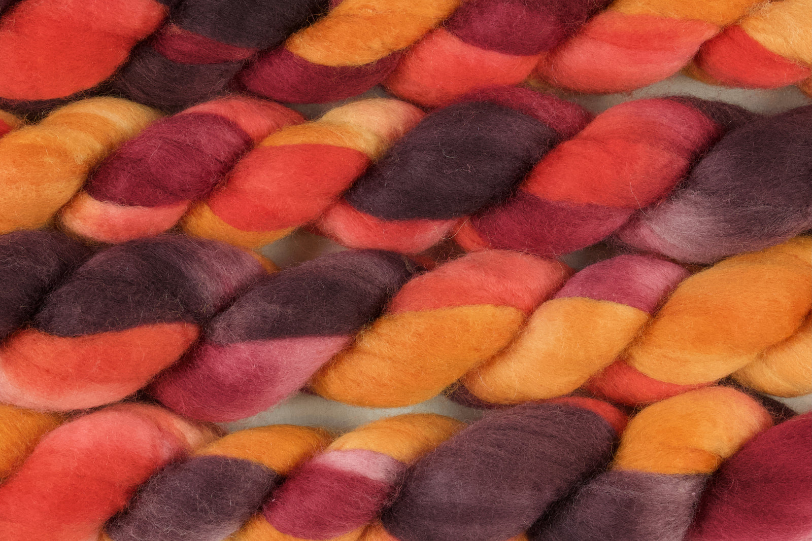 Braided fiber skein with red, orange, gold, and purple on a white background