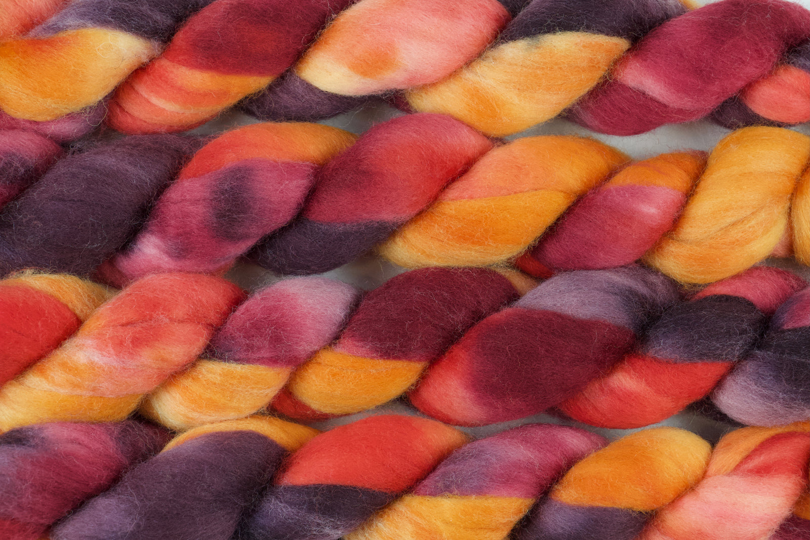 Braided fiber skein with red, orange, gold, and purple on a white background