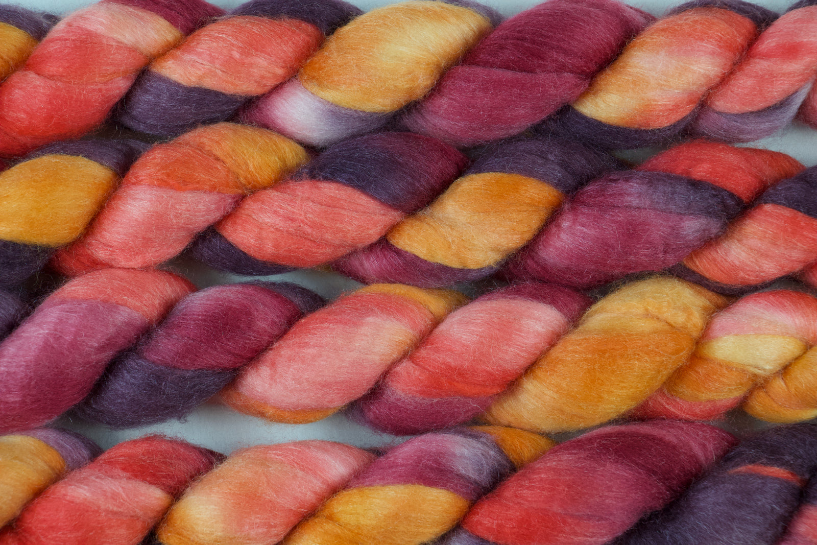 Braided fiber skein with red, orange, gold, and purple on a white background