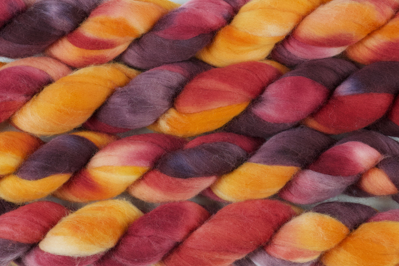 Braided fiber skein with red, orange, gold, and purple on a white background