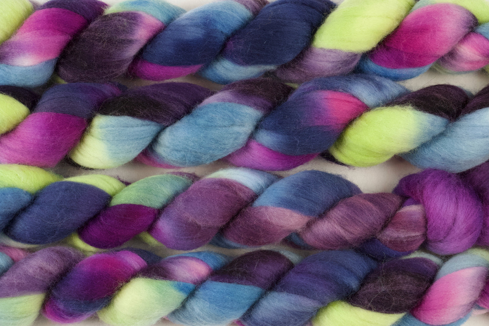 Braided fiber skein with blue, purple, pink, and green on a white background