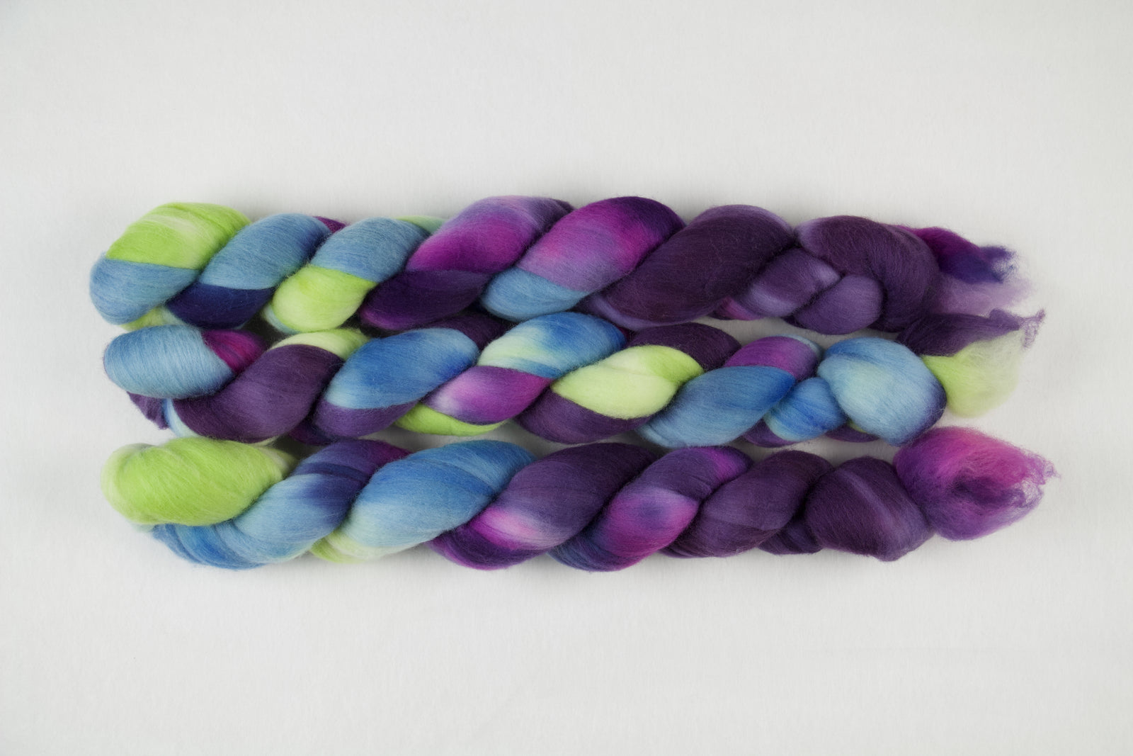 Braided fiber skein with blue, purple, pink, and green on a white background
