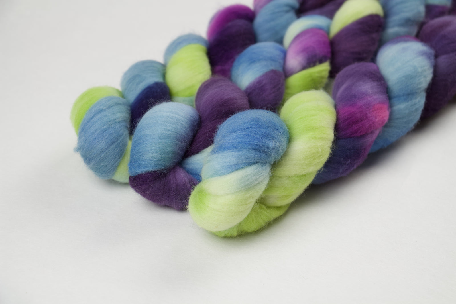 Braided fiber skein with blue, purple, pink, and green on a white background