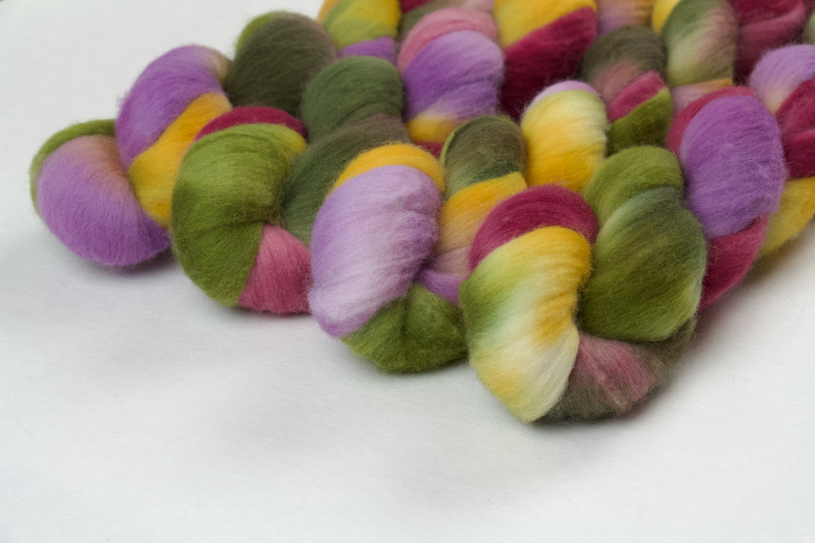 Braided fiber skein with green, pink, purple, and gold on a white background