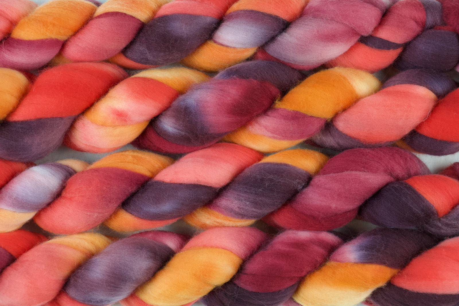 Braided fiber skein with red, orange, gold, and purple on a white background