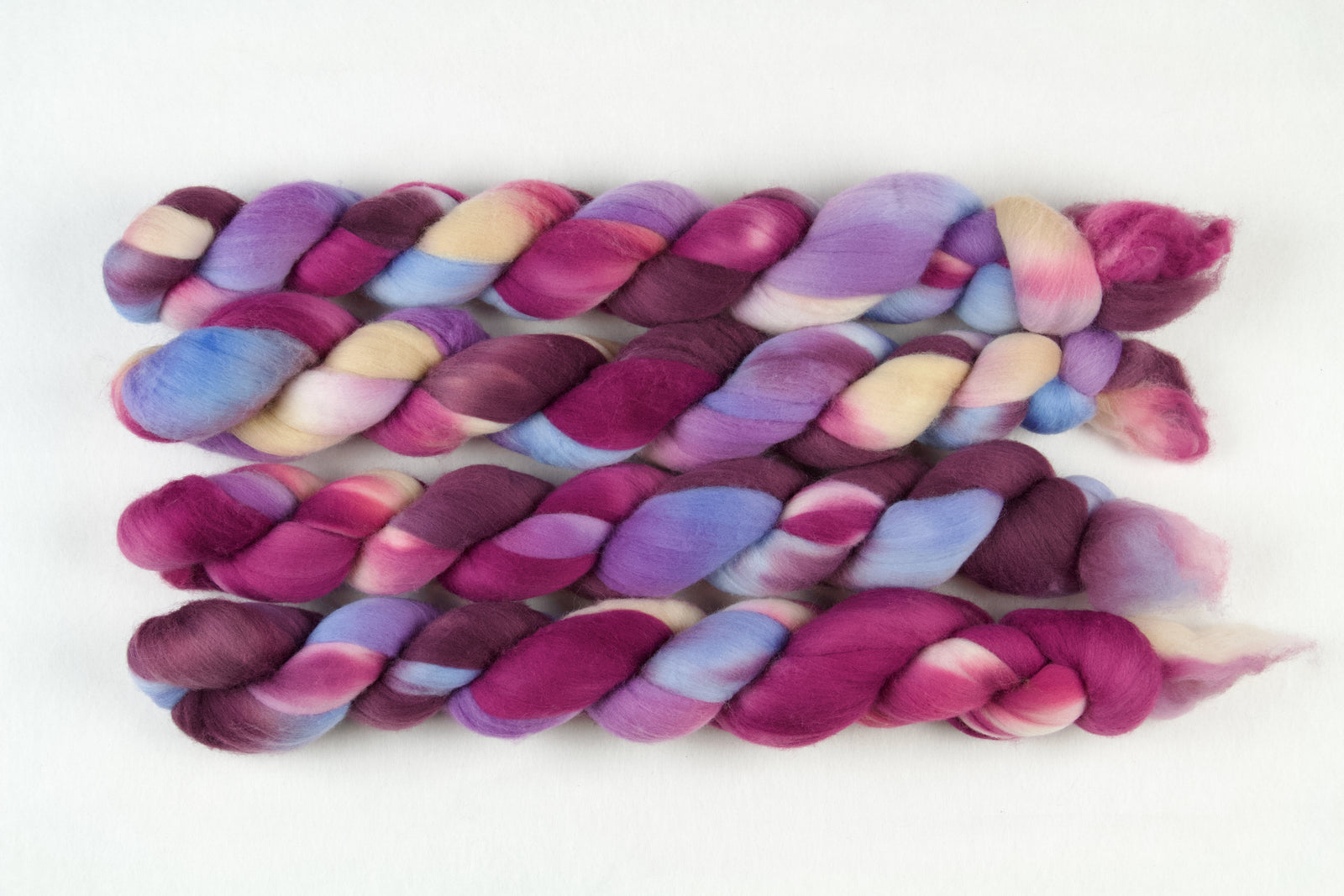 Braided fiber skein with pink, purple, blue, and champagne on a white background