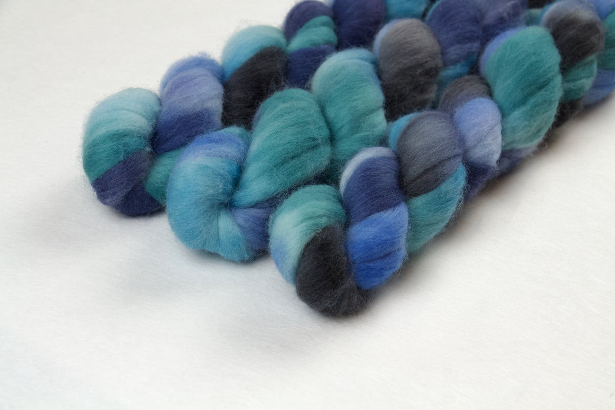 Braided fiber skein with blue, green, and grey on a white background