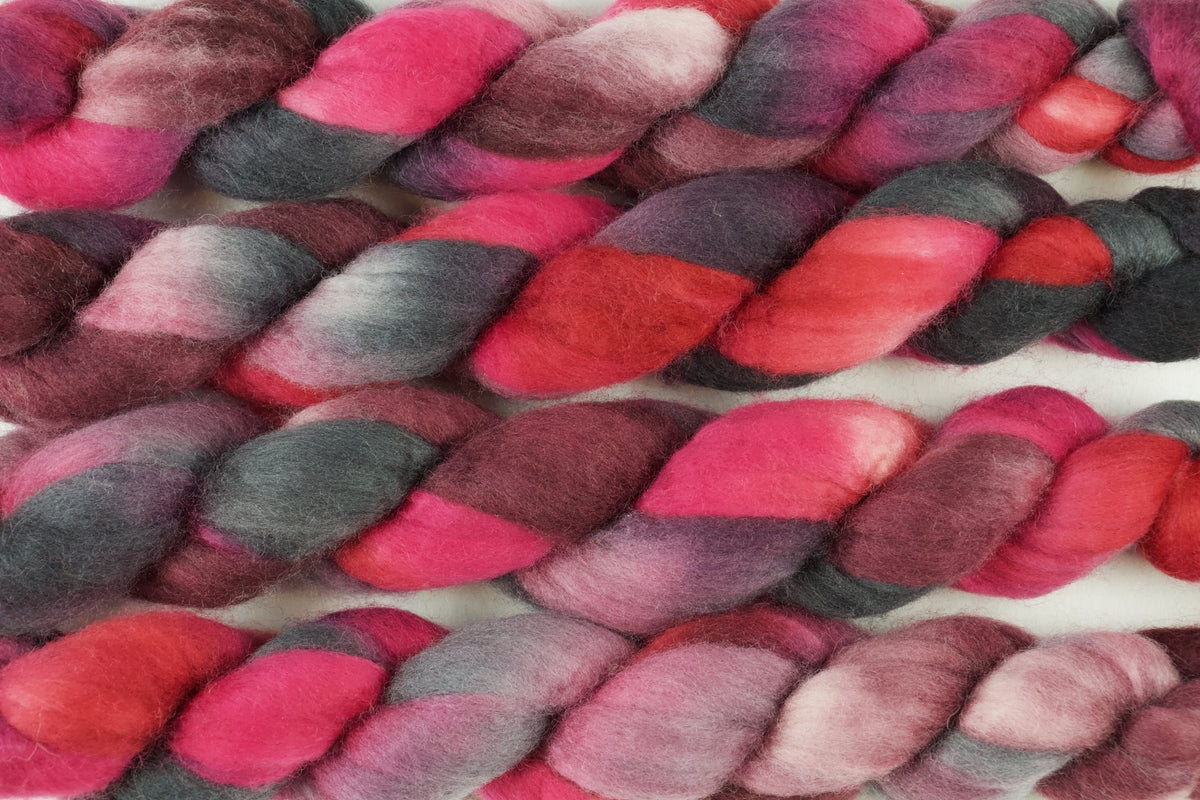 Braided fiber skein with pink, red, and black on a white background