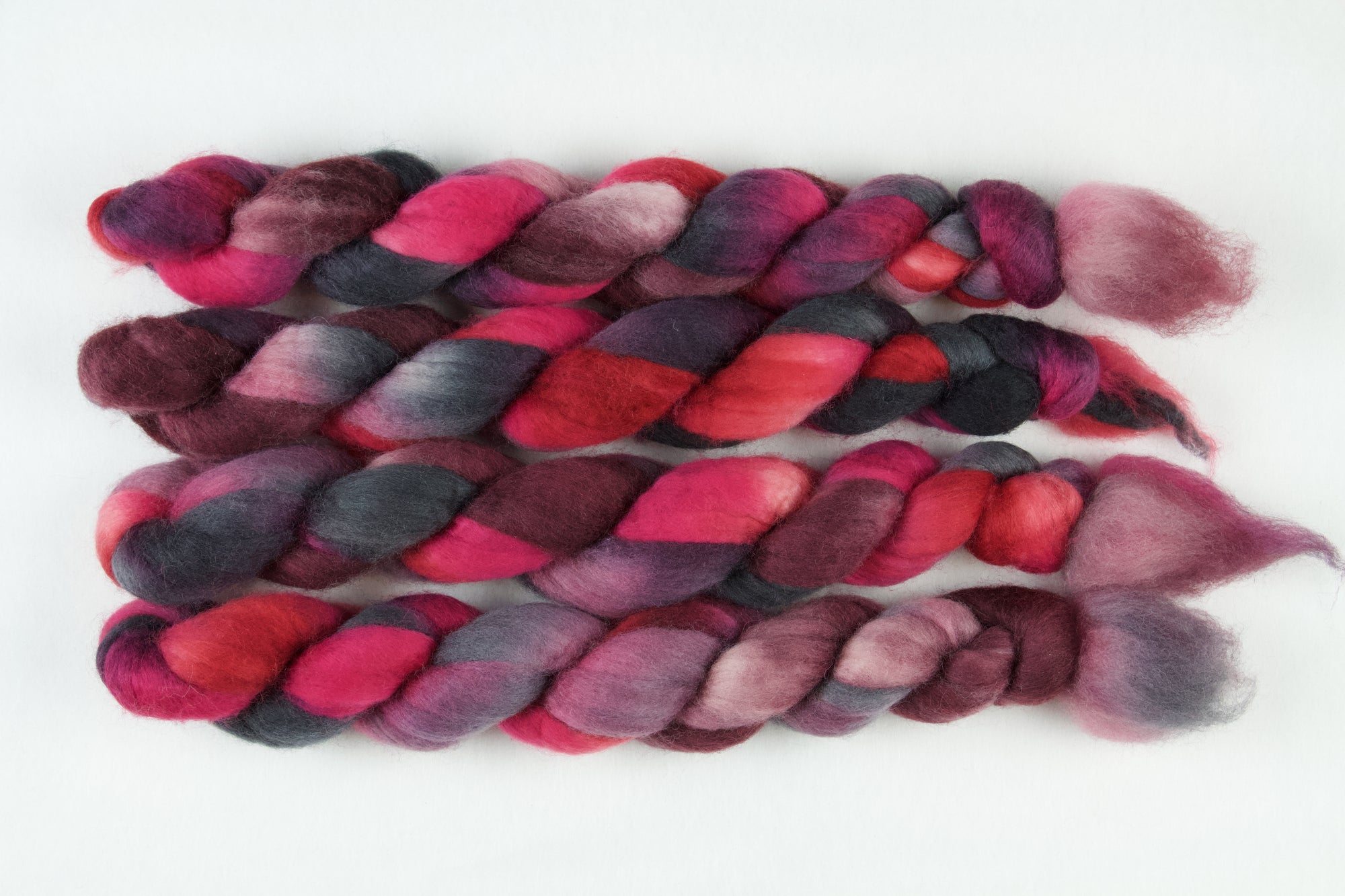 Braided fiber skein with pink, red, and black on a white background