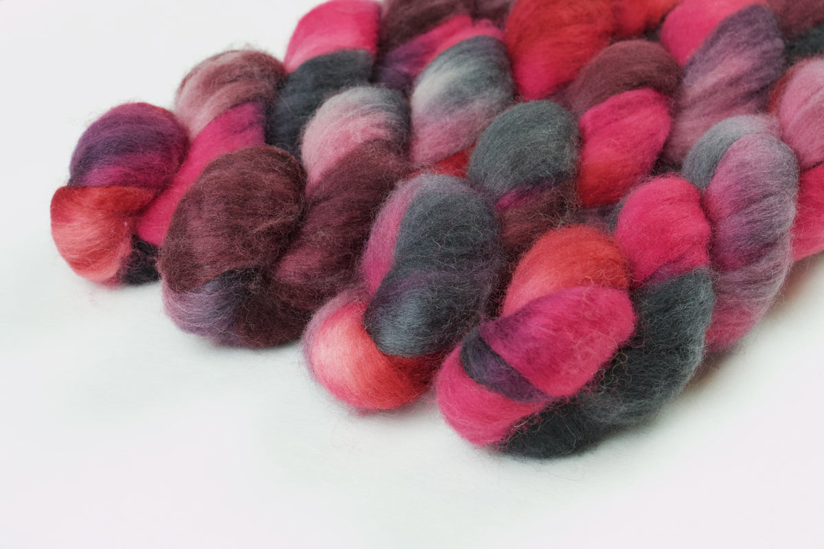Braided fiber skein with pink, red, and black on a white background