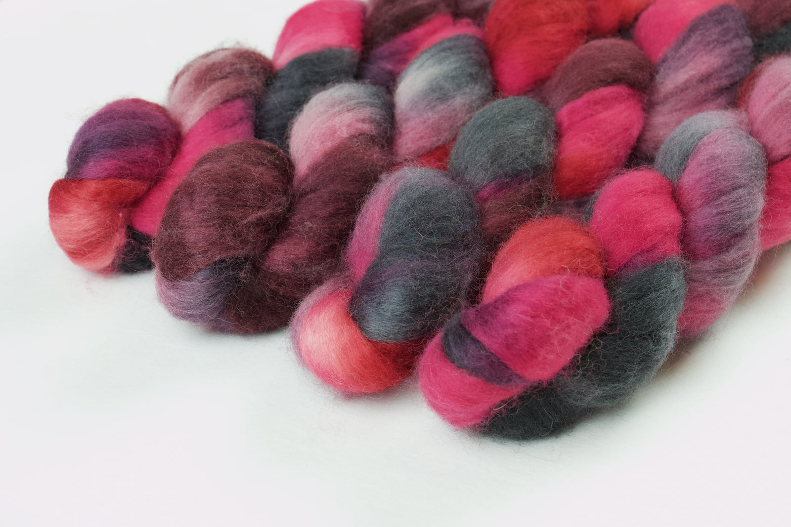 Braided fiber skein with pink, red, and black on a white background