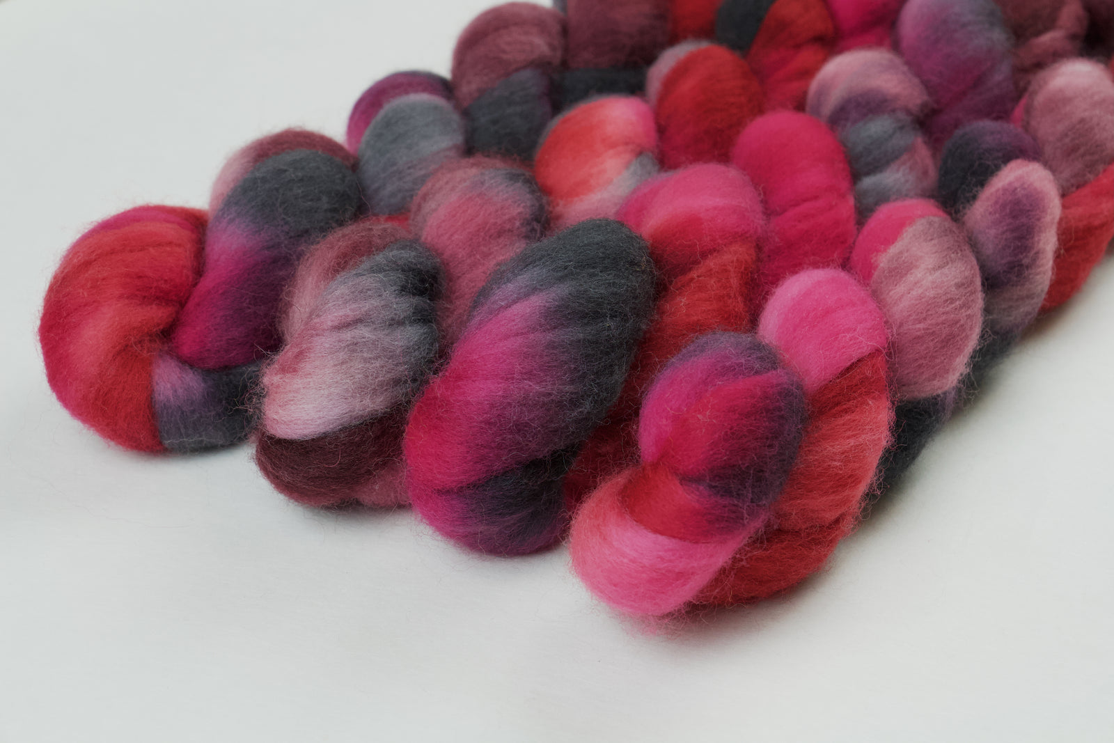 Braided fiber skein with pink, red, and black on a white background