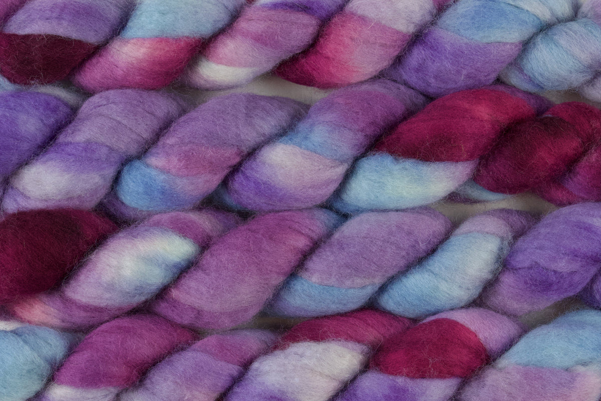 Braided fiber skein with blue, purple, and pink on a white background