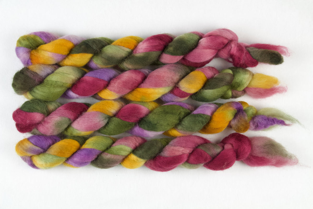 Braided fiber skein with green, pink, purple, and gold on a white background