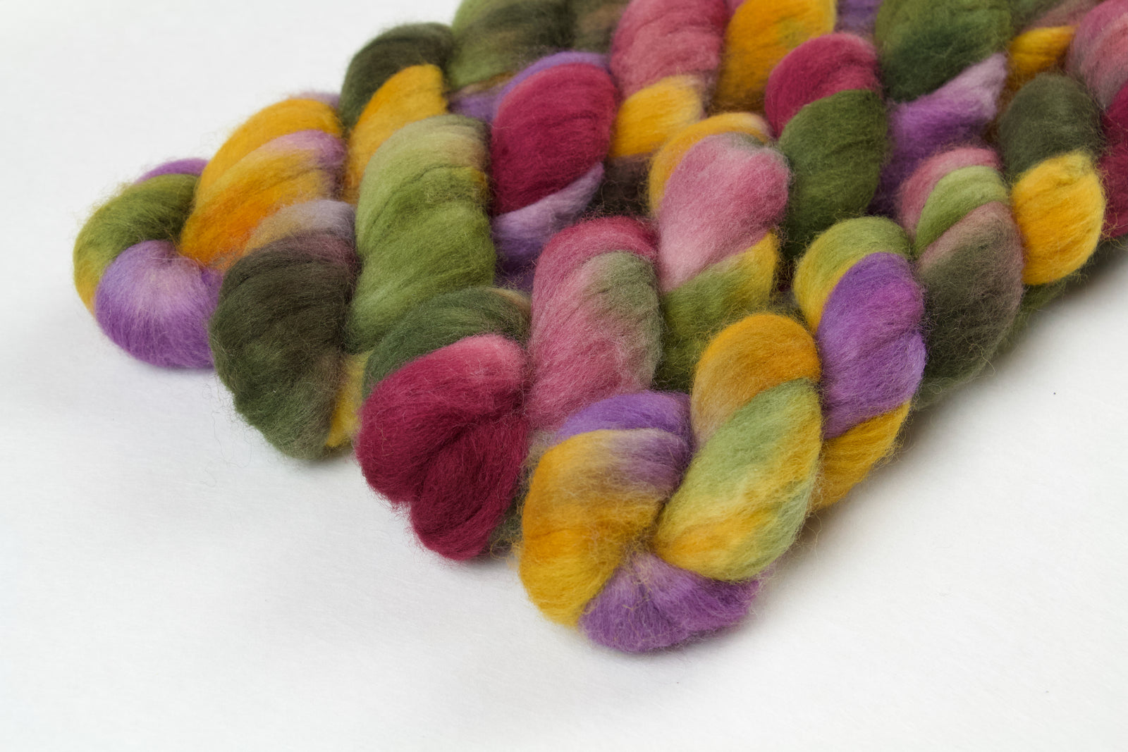 Braided fiber skein with green, pink, purple, and gold on a white background