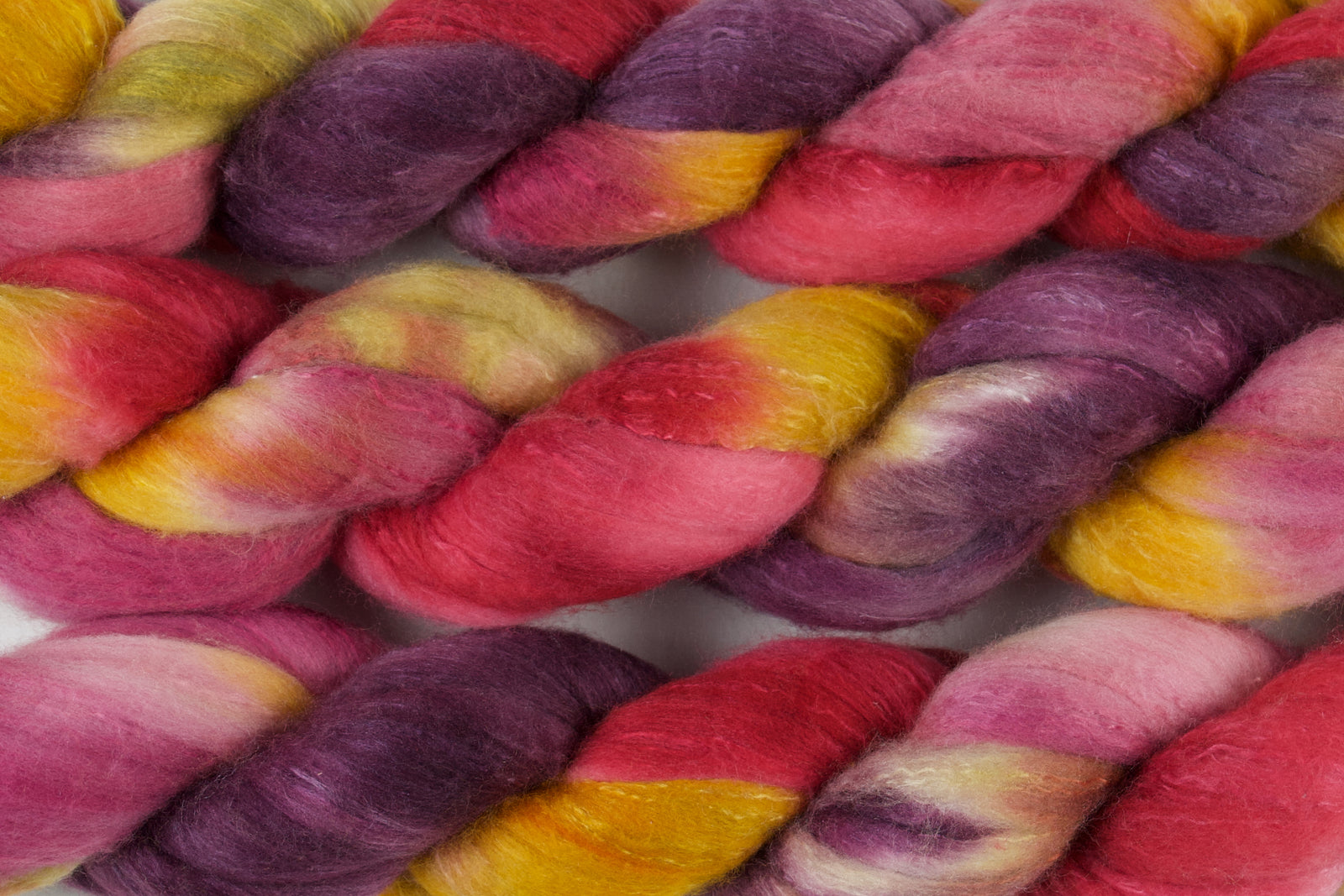Braided fiber skein with purple, red, pink, mustard, and gold on a white background