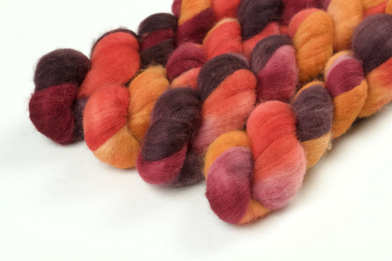 Braided fiber skein with red, orange, gold, and purple on a white background