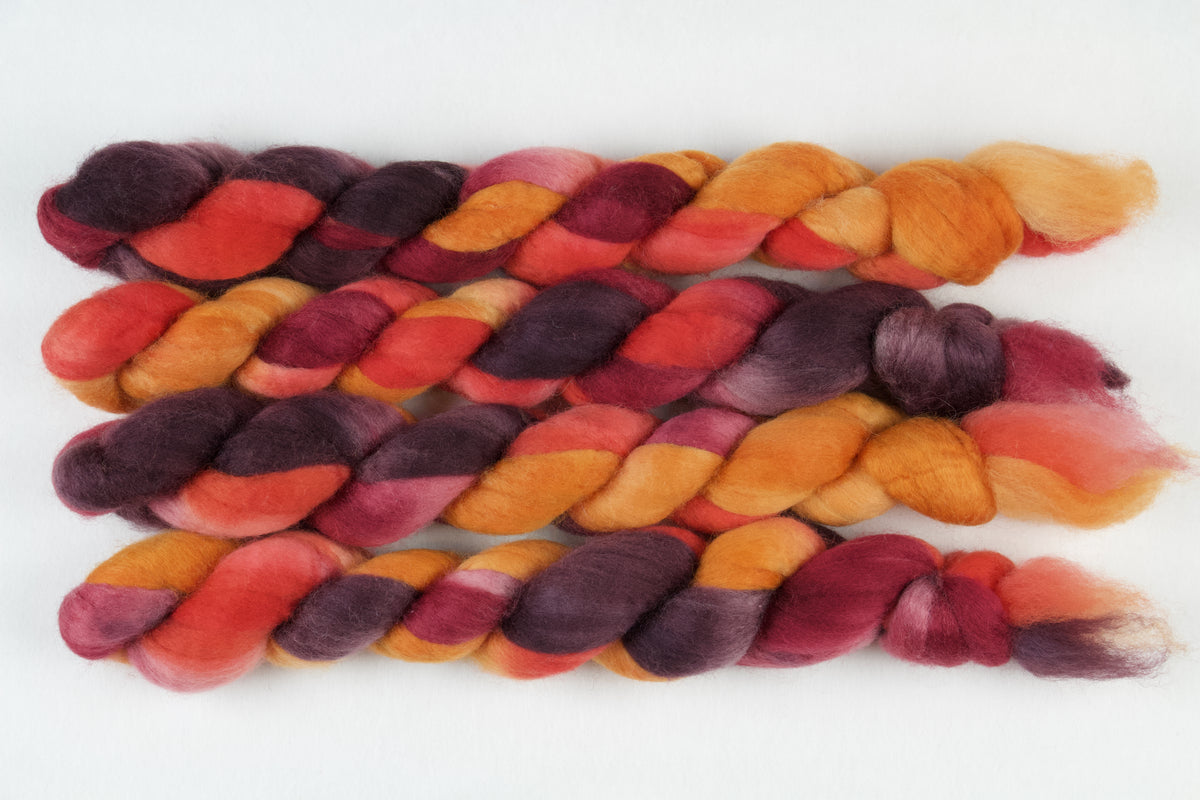 Braided fiber skein with red, orange, gold, and purple on a white background