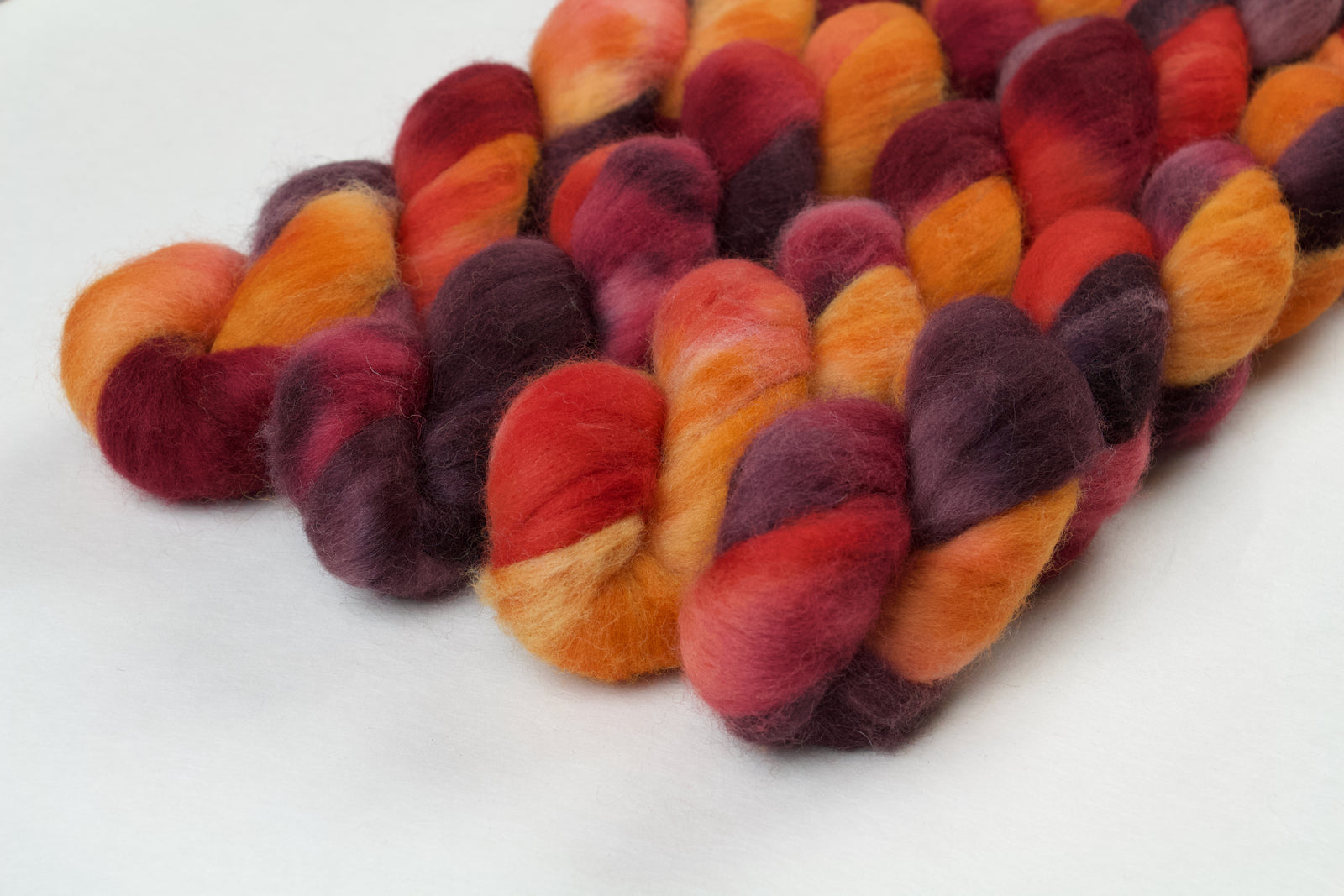 Braided fiber skein with red, orange, gold, and purple on a white background