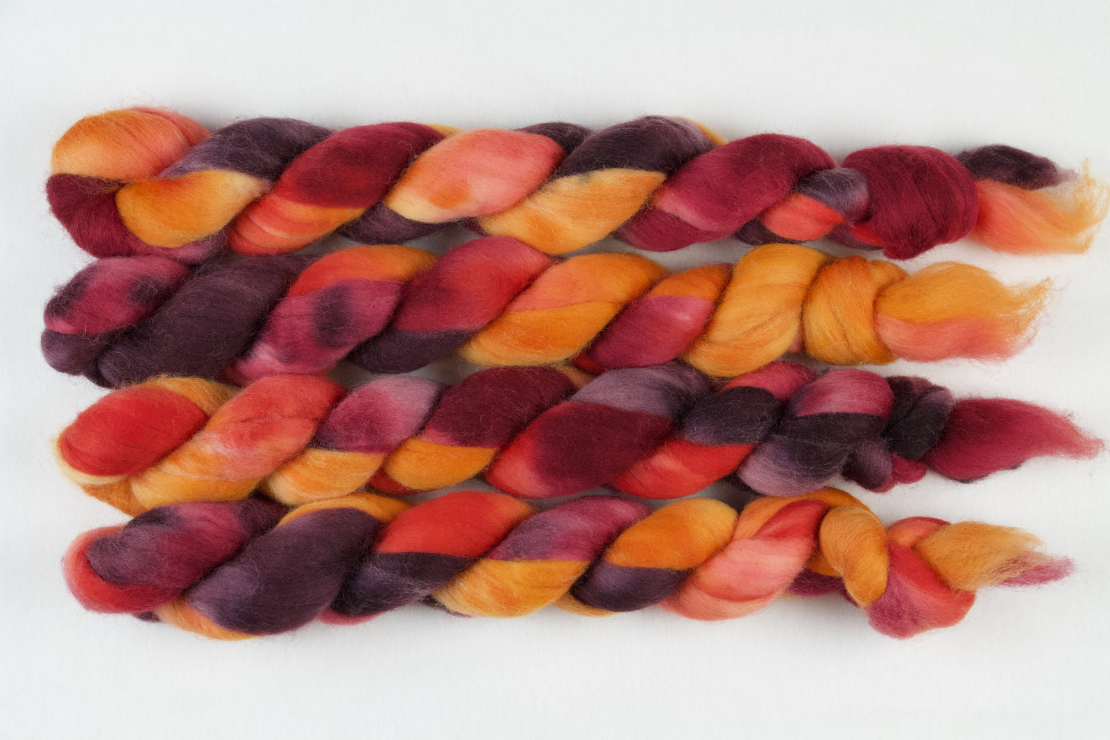 Braided fiber skein with red, orange, gold, and purple on a white background