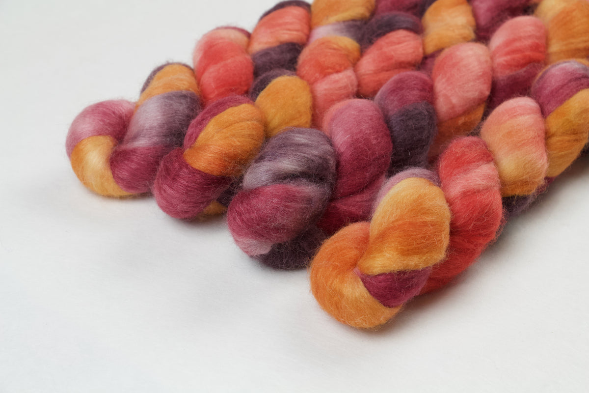 Braided fiber skein with red, orange, gold, and purple on a white background