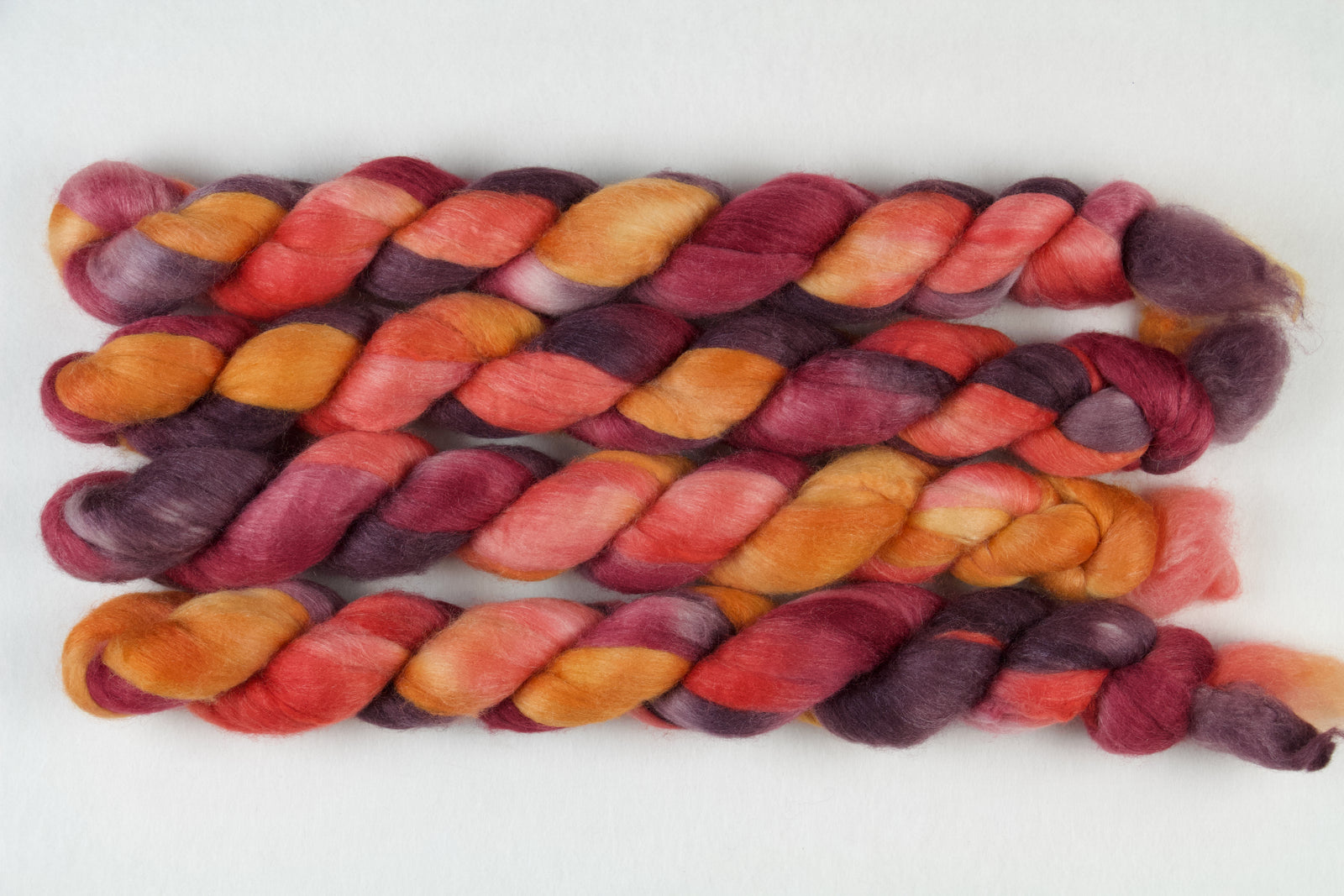 Braided fiber skein with red, orange, gold, and purple on a white background
