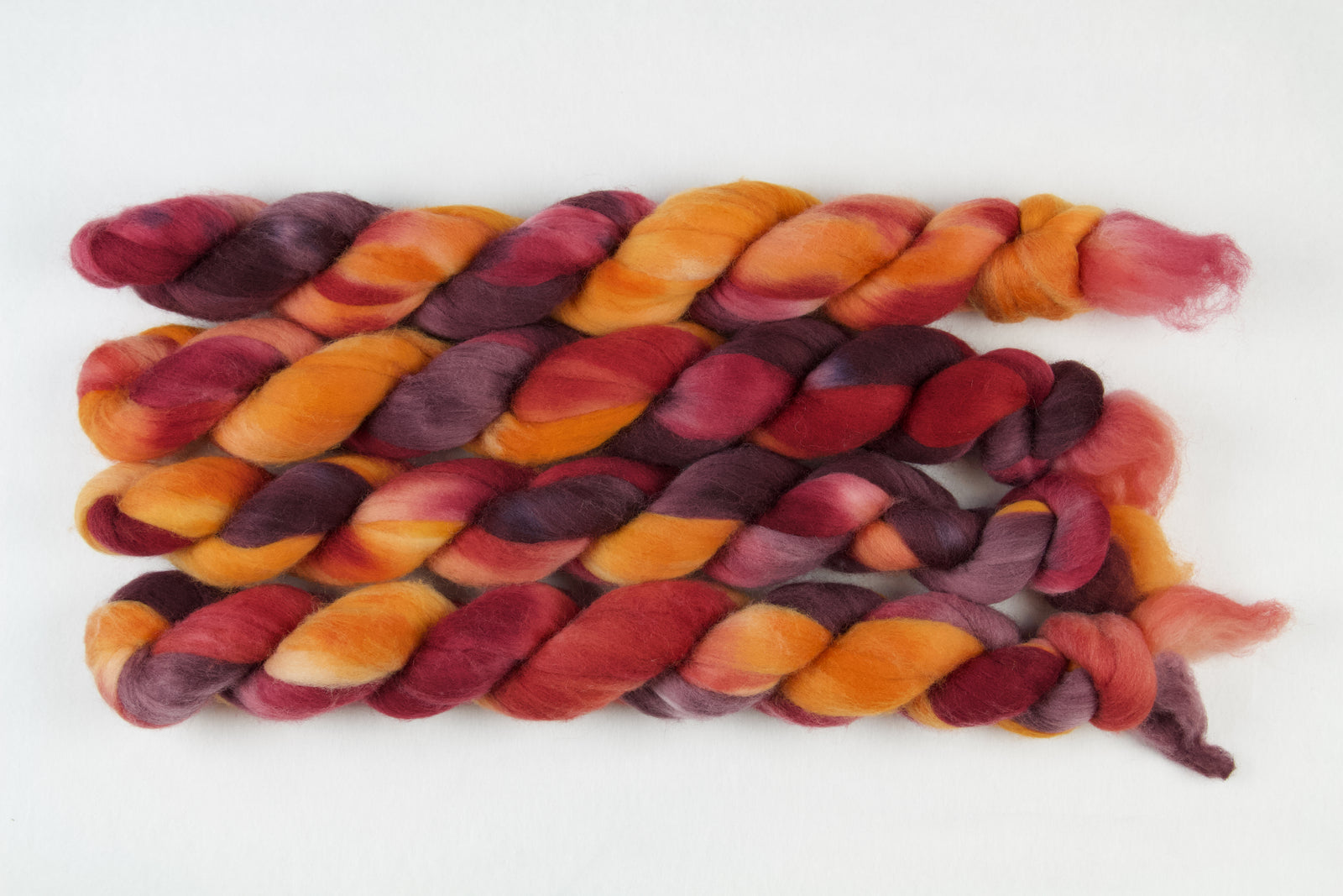 Braided fiber skein with red, orange, gold, and purple on a white background