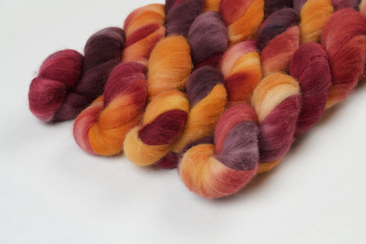 Braided fiber skein with red, orange, gold, and purple on a white background