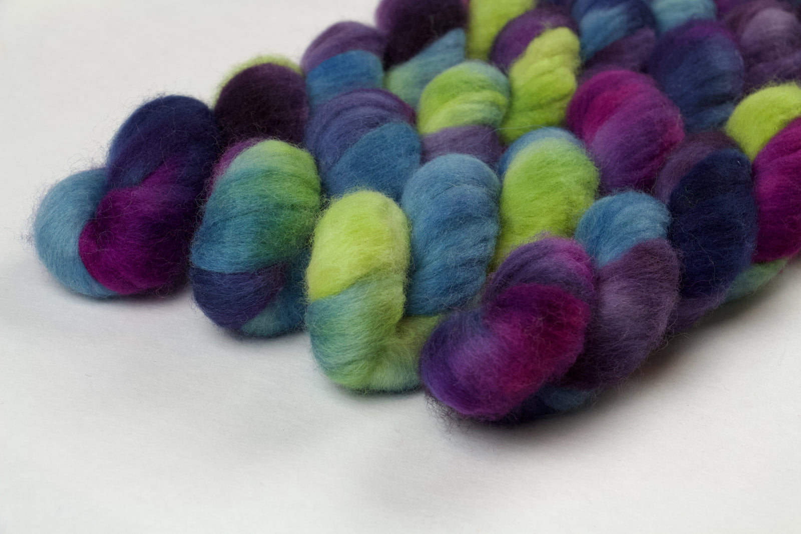 Braided fiber skein with blue, purple, pink, and green on a white background