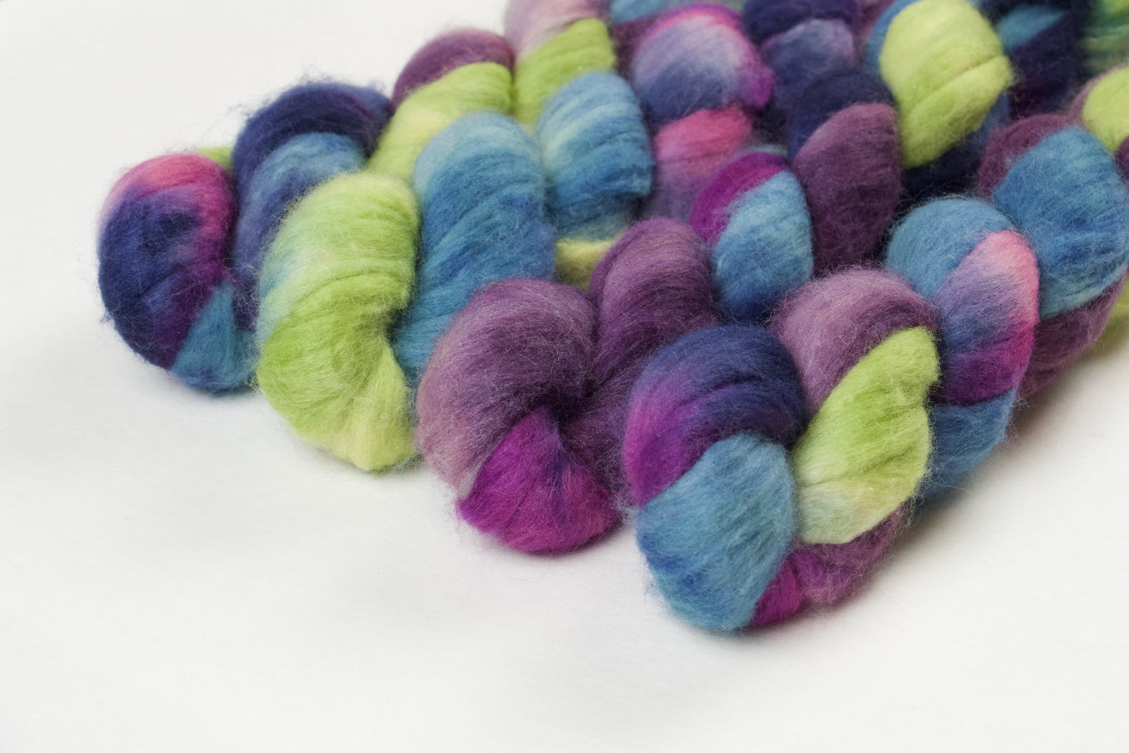 Braided fiber skein with blue, purple, pink, and green on a white background