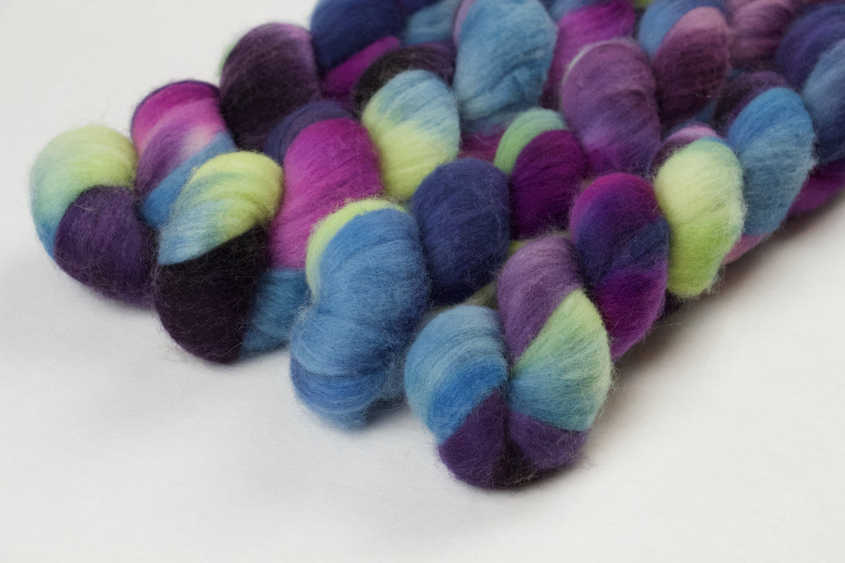 Braided fiber skein with blue, purple, pink, and green on a white background