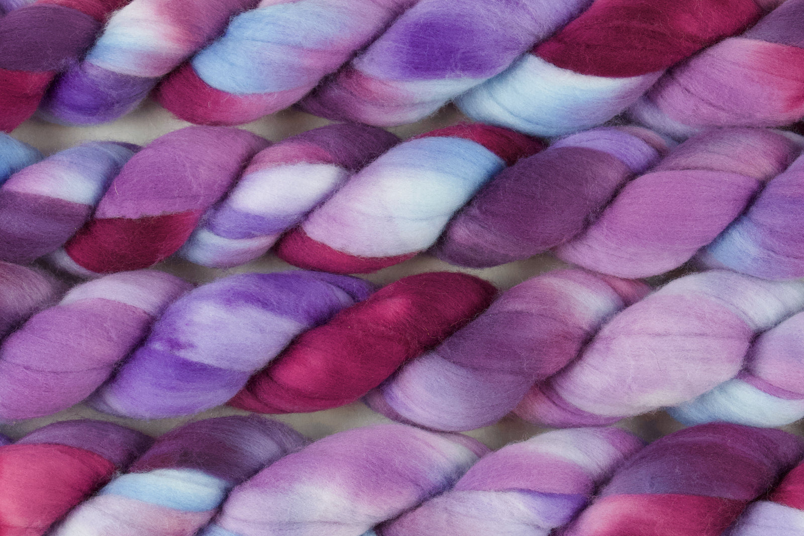 Braided fiber skein with blue, purple, and pink on a white background