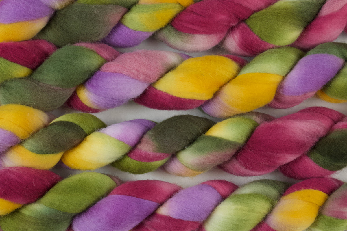 Braided fiber skein with green, pink, purple, and gold on a white background