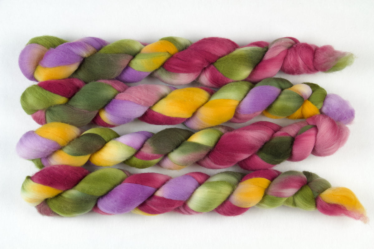 Braided fiber skein with green, pink, purple, and gold on a white background