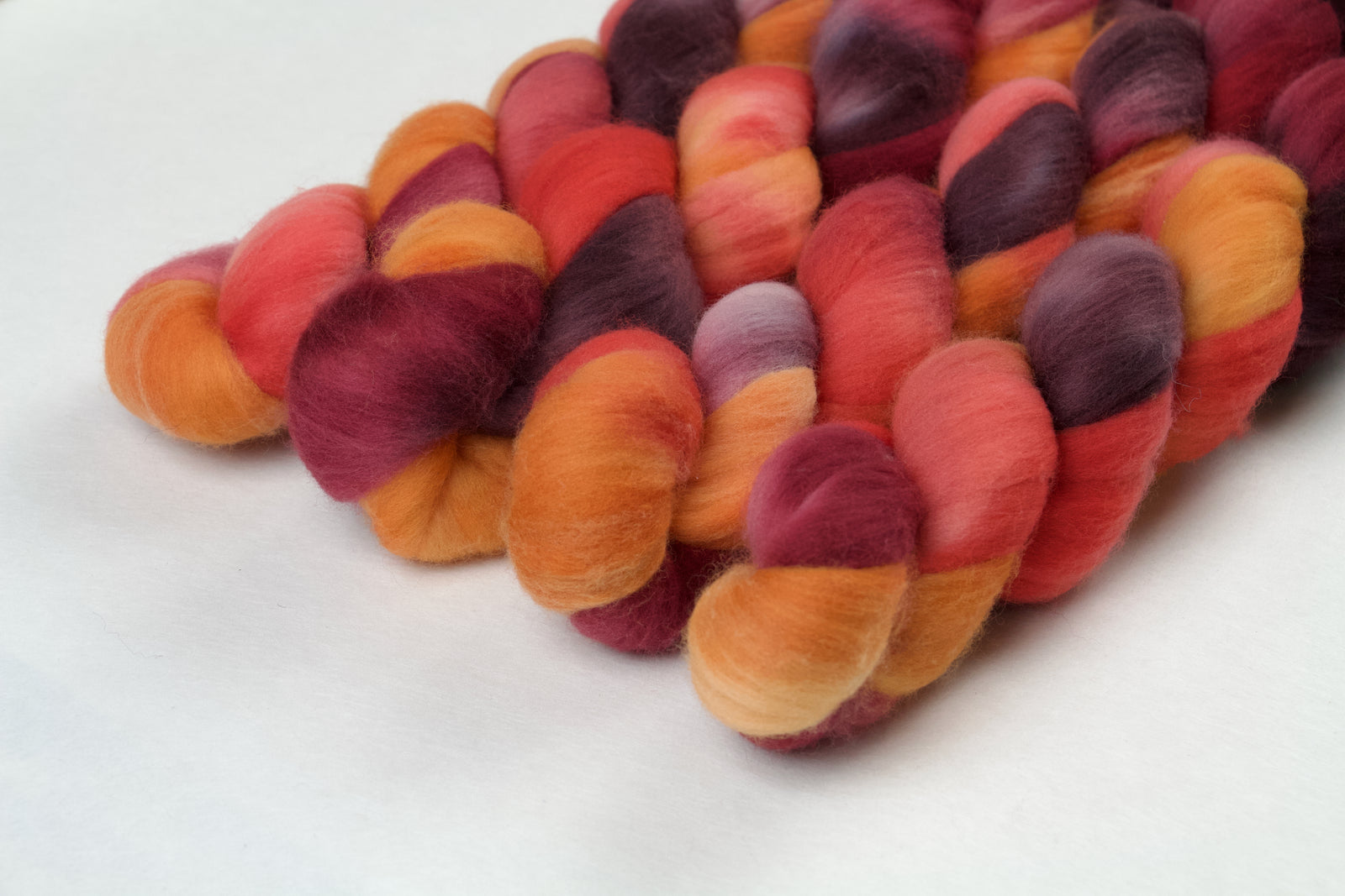Braided fiber skein with red, orange, gold, and purple on a white background