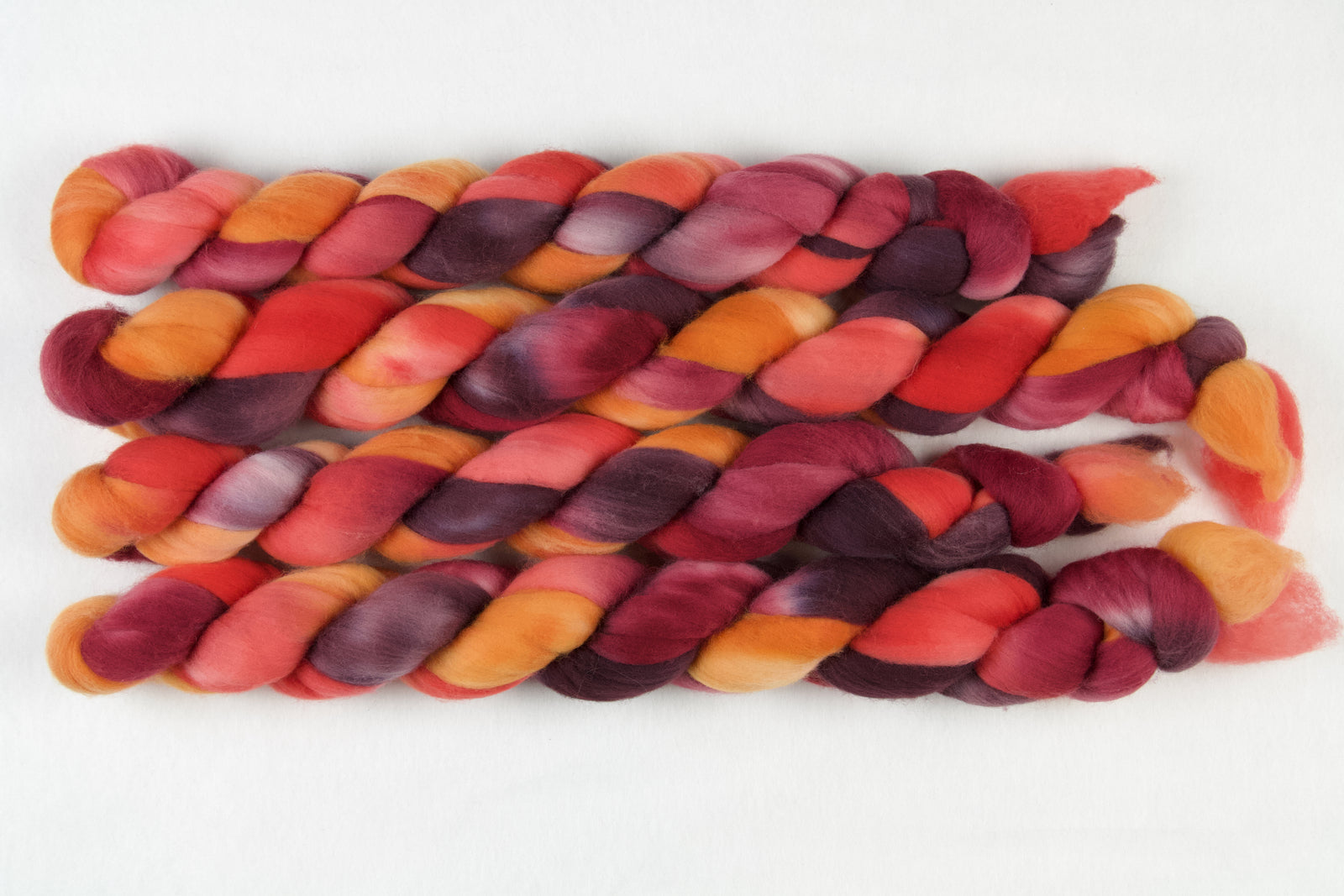 Braided fiber skein with red, orange, gold, and purple on a white background