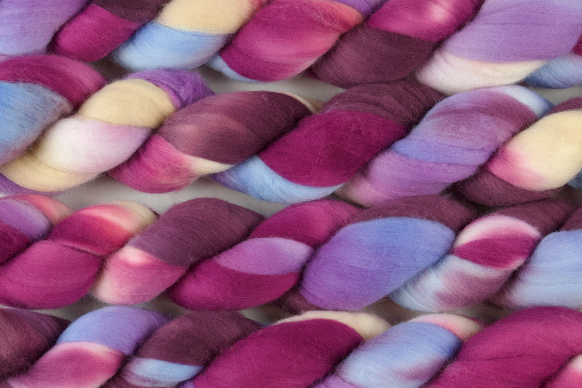Braided fiber skein with pink, purple, blue, and champagne on a white background
