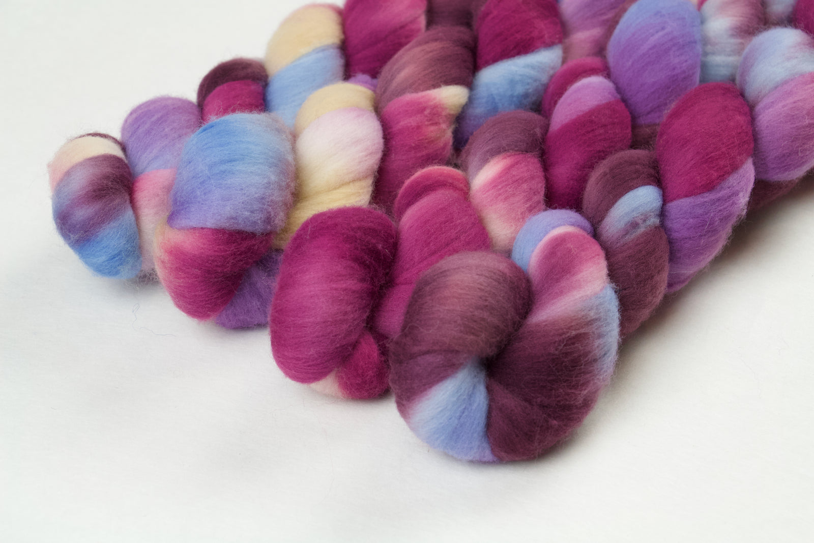 Braided fiber skein with pink, purple, blue, and champagne on a white background