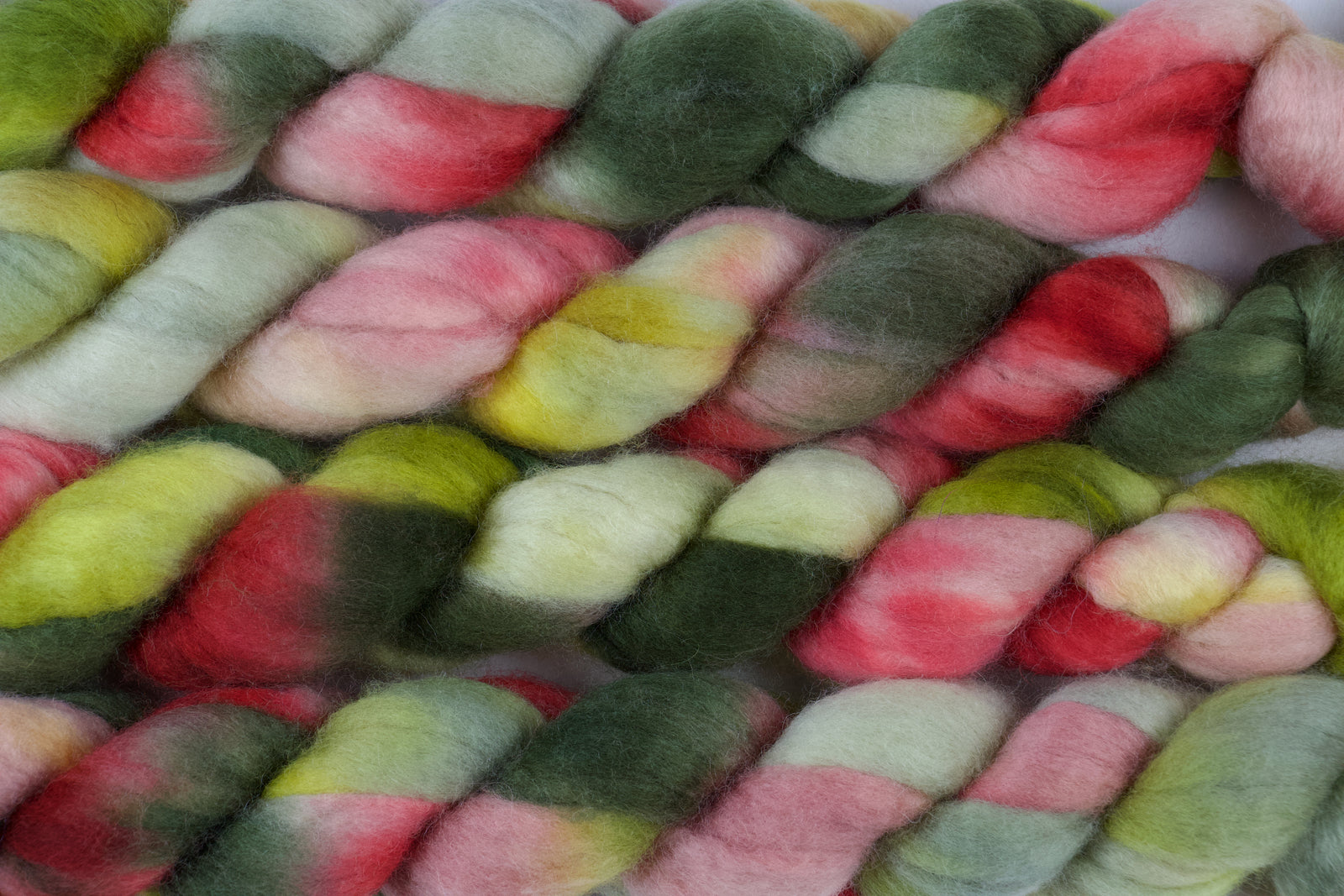 Braided fiber skein with pink, red, and green on a white background
