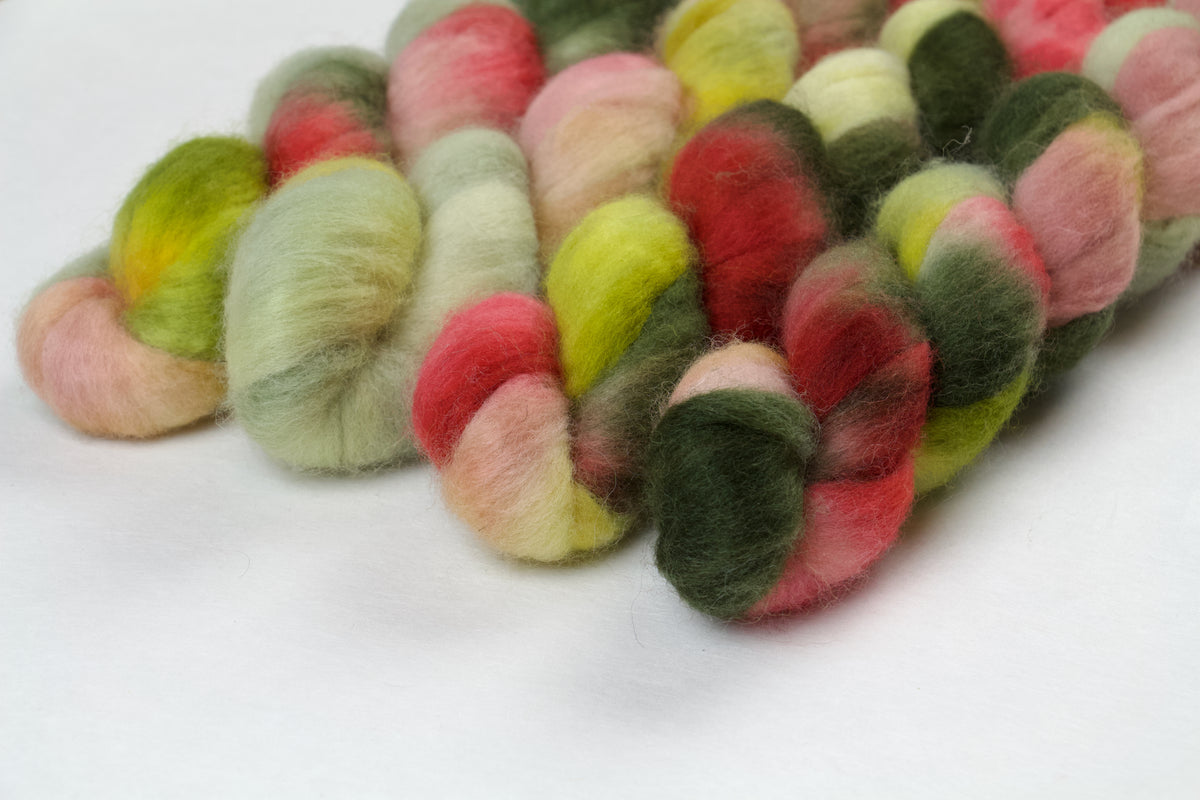 Braided fiber skein with pink, red, and green on a white background