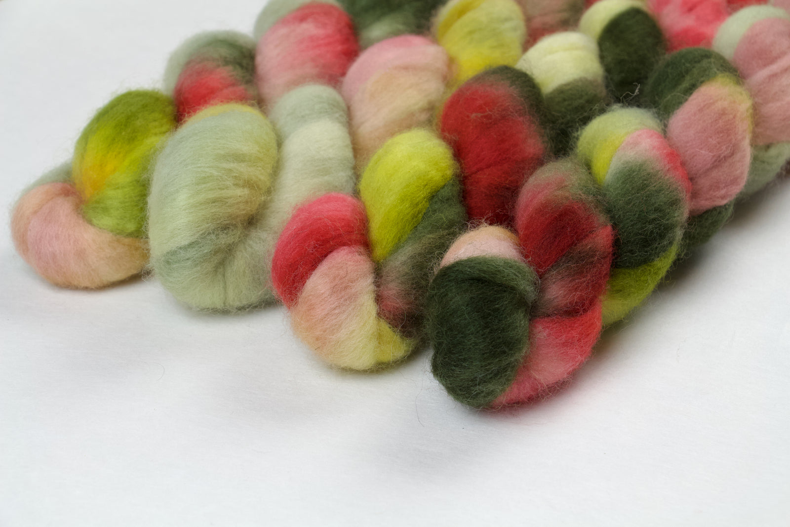Braided fiber skein with pink, red, and green on a white background