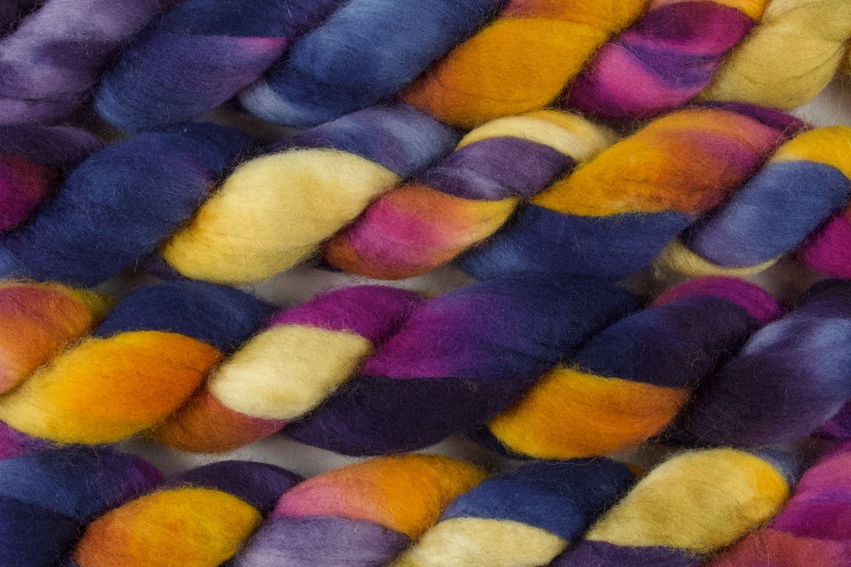 Braided fiber skein with blue, purple, pink, and gold on a white background